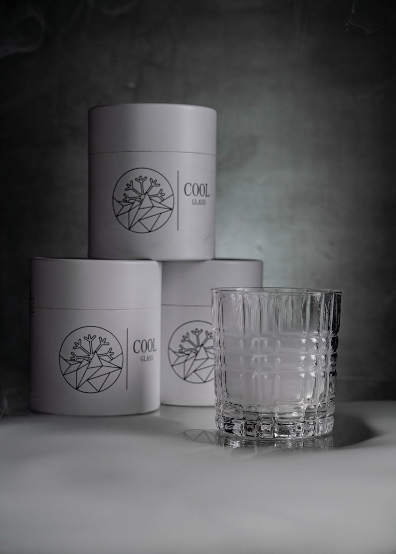 Modernes Whiskeyglas mit strukturiertem Design vor minimalistischer Verpackung mit CoolGlass Logo