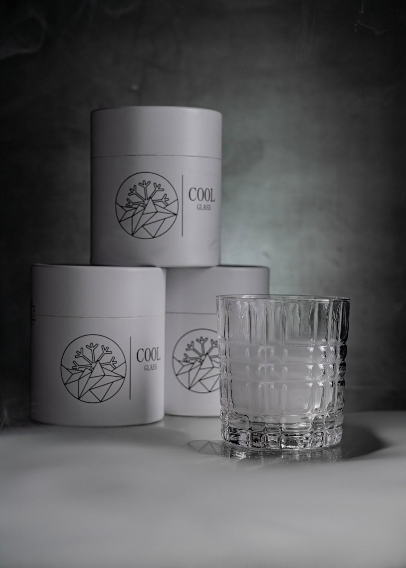 Modernes Whiskeyglas mit strukturiertem Design vor minimalistischer Verpackung mit CoolGlass Logo